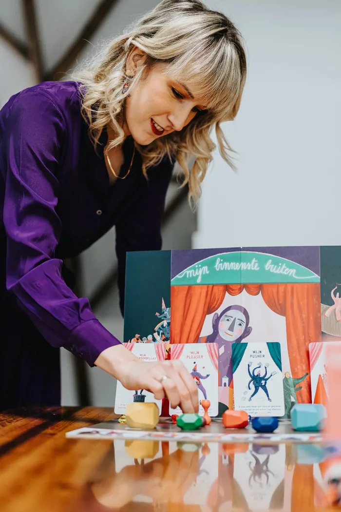 Een hand zet een houten figuurtje naast het theatertje met spelerskaarten
