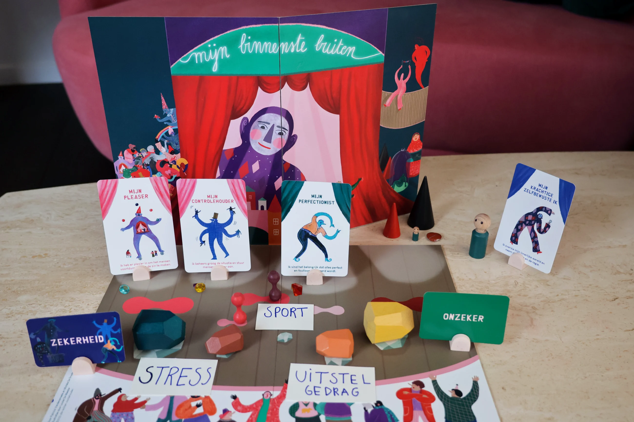De volledige opstelling op tafel: het opengevouwen opstellingsbord met het theater, toneelspelerkaarten in houders, houten struikelblokken, halters, kegels, popjes, parels en het hartje.